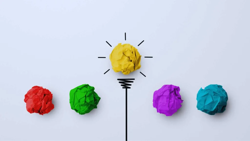 A collection of colorful crumpled paper balls, with a yellow one positioned as a lightbulb, symbolizing creative ideas, learning, and insights for beginners starting their keto journey