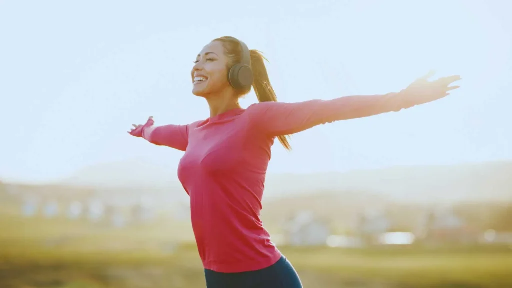 A happy woman in a bright outdoor setting, stretching her arms wide with a joyful smile, symbolizing freedom, new beginnings, and the excitement of taking the first step into a keto lifestyle.