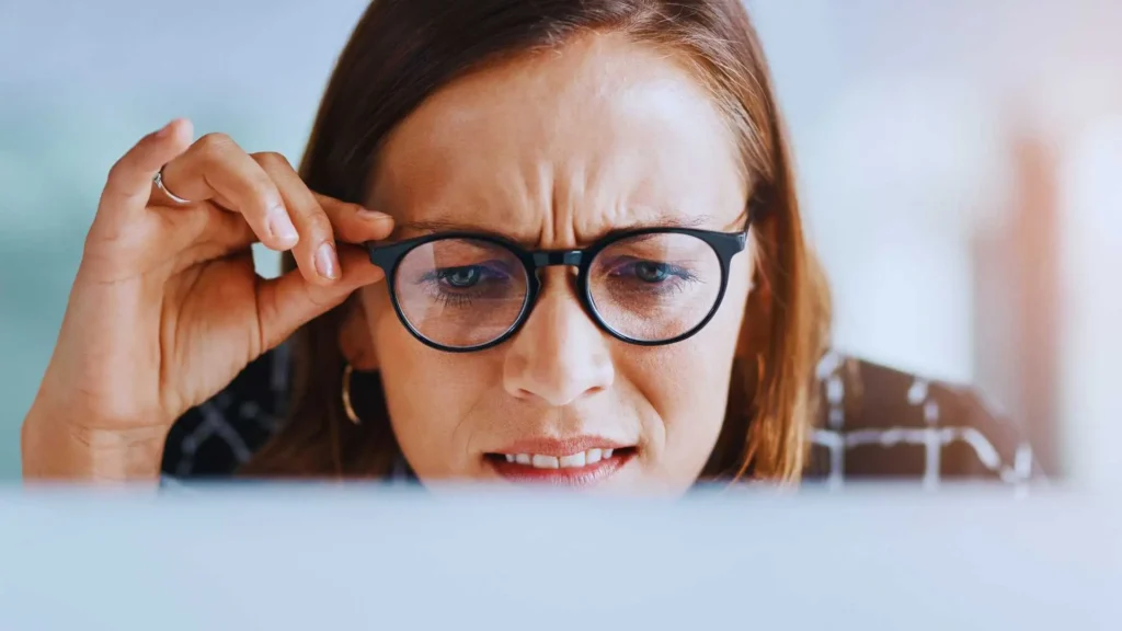 A focused woman adjusting her glasses while looking at a screen, symbolizing deep thought and understanding. The bright background represents clarity and learning about the keto diet