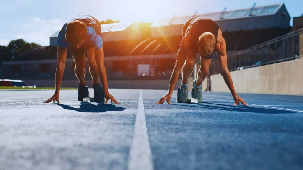 Two athletes crouched at the starting line, ready to sprint, with sunlight shining over the track. The image symbolizes taking the first step, commitment, and the beginning of a journey, representing how to get started with keto